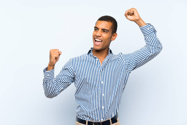 Young handsome brunette man over isolated blue background celebrating a victory - Фото, изображение
