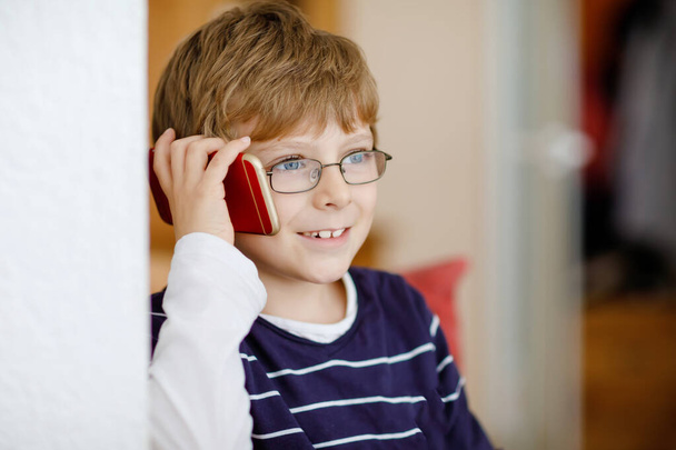Χαριτωμένο αγοράκι με γυαλιά που μιλάει στο κινητό. Αξιολάτρευτο υγιές παιδί κρατώντας smartphone και μιλώντας με ένα κορίτσι φίλο ή με τους γονείς, παππούδες. - Φωτογραφία, εικόνα