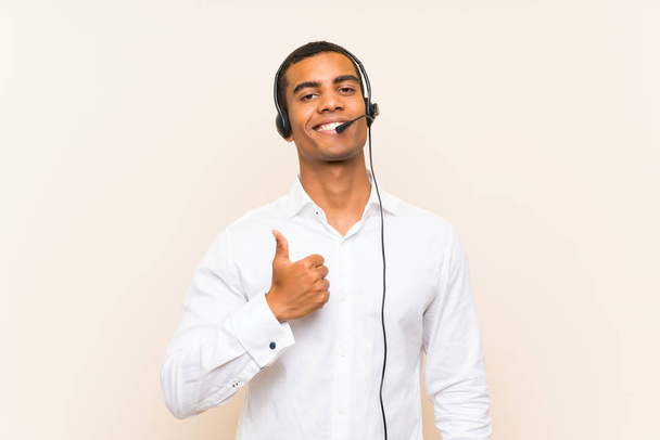 Egy fiatal barna férfi feltartott hüvelykujjú fülhallgatóval dolgozik, mert valami jó dolog történt. - Fotó, kép