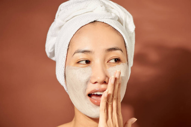 Heureuse jeune femme asiatique appliquant un masque d'argile sur son visage sur fond orange. Gros plan.  - Photo, image