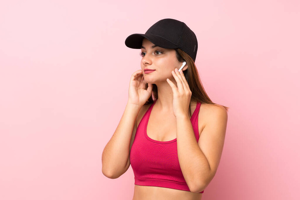 Young sport girl over isolated pink background listening music - Foto, Imagen