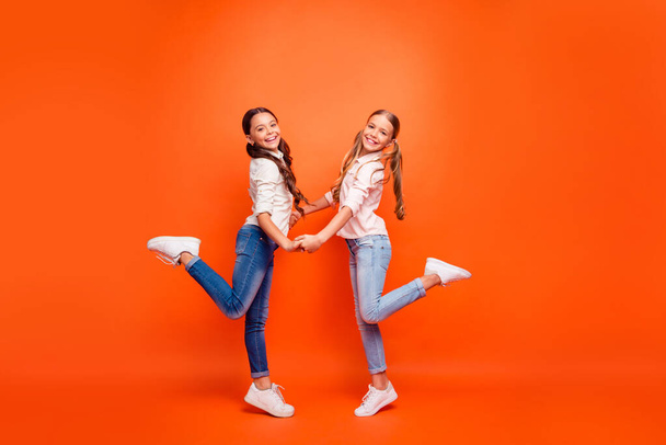 Full length profile side photo of positive two children girls rest autumn holidays rest relax hold hands wear white modern outfit isolated over orange color background - Fotografie, Obrázek