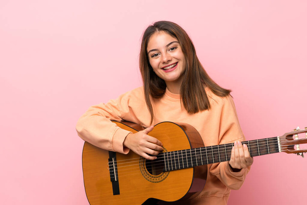 jong brunette meisje met gitaar over geïsoleerde roze achtergrond - Foto, afbeelding