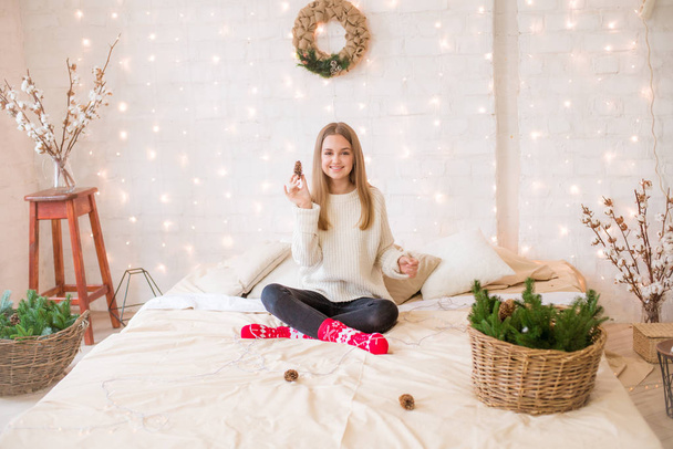 Cute teenage girl has fun at home in a light loft on the bed, decorated for Christmas with garlands and needles. Christmas mood - Fotografie, Obrázek
