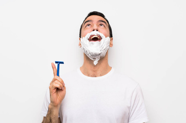 Muž holení jeho vousy přes izolované bílé pozadí ukazuje nahoru a překvapen - Fotografie, Obrázek