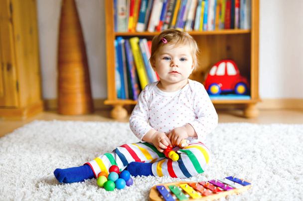 自宅や保育園で教育用のおもちゃで遊ぶ愛らしいかわいい赤ちゃんの女の子。カラフルな音楽おもちゃの木琴で楽しい時間を過ごしている幸せな健康的な子供異なるスキルを学ぶ子供 - 写真・画像