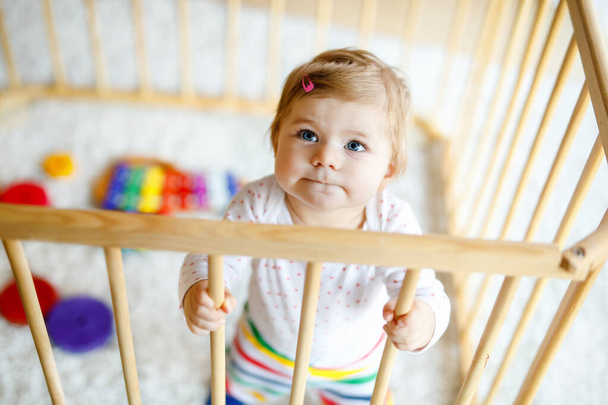 Beautiful little baby girl standing inside playpen. Cute adorable child playing with colorful toys. Home or nursery, safety for kids. Alone baby waiting for mom - Photo, Image