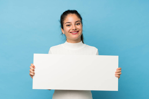 Young brunette girl over isolated blue background holding an empty white placard for insert a concept - Fotoğraf, Görsel