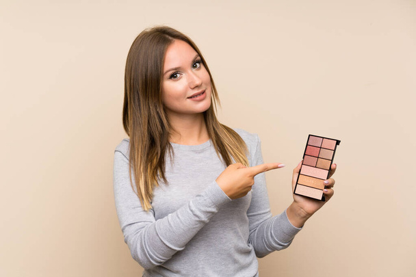 Teenager girl with makeup palette over isolated background and pointing it - Photo, Image