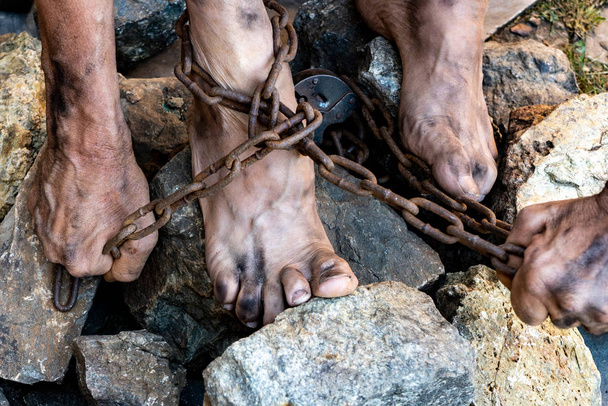 Dirty slave legs in chains among stones. Slave in an attempt to free himself. The symbol of slave labor - Foto, Imagen