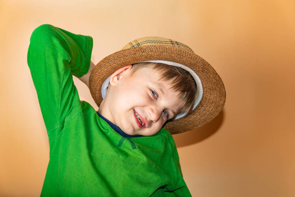 Niño alegre y feliz en un sombrero de paja y ropa verde sonriendo y mirando a la cámara
. - Foto, imagen