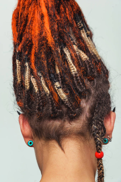 Girl with red fire dreadlocks gathered in a tail on a white background rear view. A young woman with long dreadlocks on her head. Girl informal looks with orange dreadlocks and piercings close up - Photo, Image