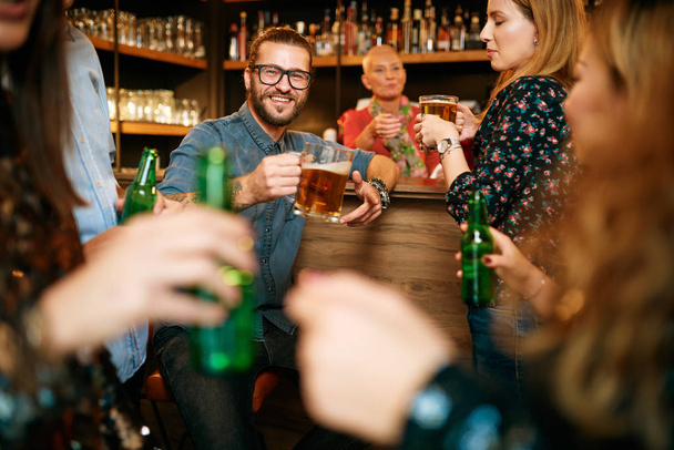 Grupo de amigos bebiendo cerveza, charlando y divirtiéndose en el pub. Noche fuera.
. - Foto, Imagen