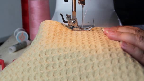woman sews texture fabric on a modern sewing machine while sitting at home on a gray sofa, hobby and needlework concept, close-up - Кадры, видео