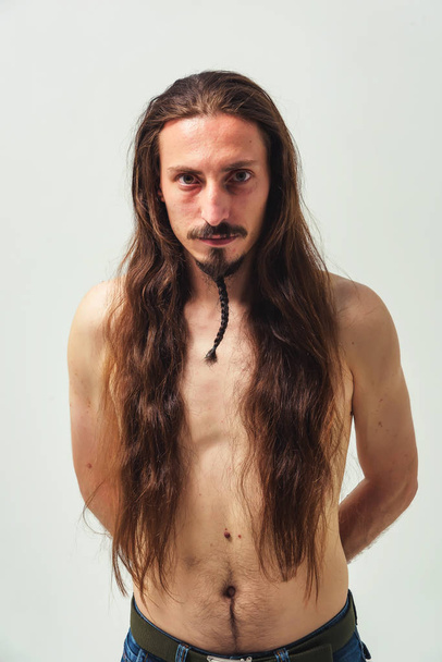A man with long hair and a beard with a naked torso on a white background. Long flowing hair of a young boy. Care for long men's hair - Foto, Imagem
