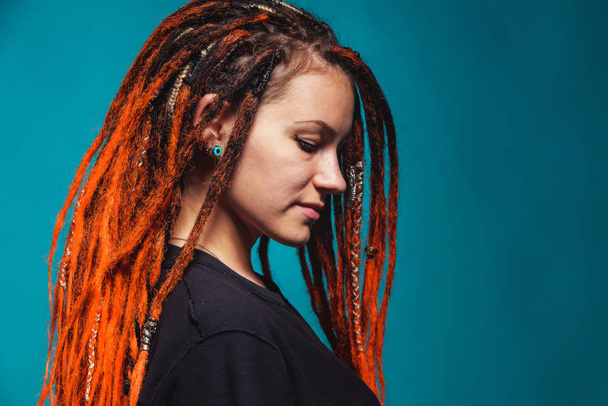 Girl with red fire dreadlocks on sea wave background color. A young woman with orange dreadlocks and piercings on a blue background. Beautiful daring informal image of a girl with red yellow dreadlocks - Photo, Image