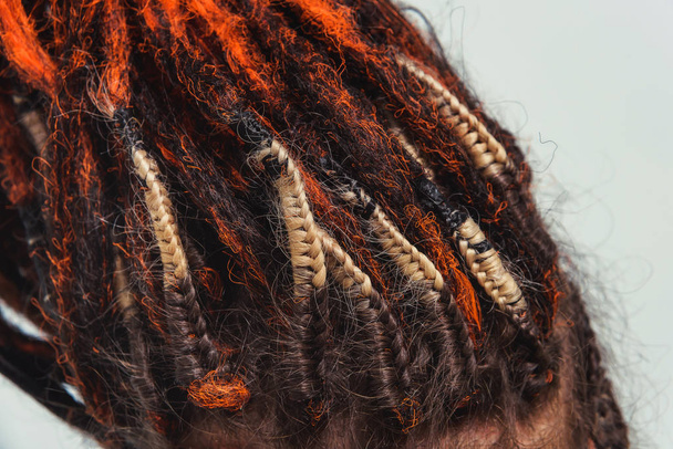 Red fiery natural dreadlocks and pigtails with decorations at the scalp. Orange dreadlocks and close-up jewelry. Artificial dreadlocks for hair collected in a ponytail. Braiding and fastening dreadlocks to hair - Photo, Image