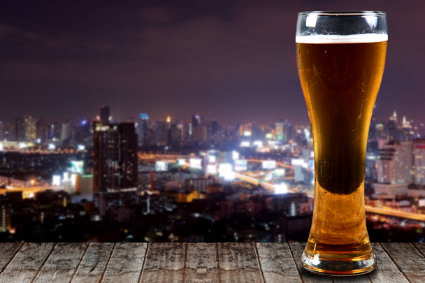 Glass of beer on a wooden City at night background. - Photo, Image