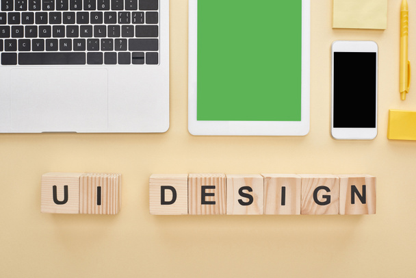 flache Lage mit Gadgets und Holzklötzen mit UI-Design-Schriftzug auf gelbem Hintergrund - Foto, Bild