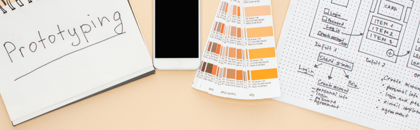 bovenaanzicht van smartphone in de buurt van website design sjabloon, kleurenpalet en notebook met prototyping belettering op beige achtergrond, panoramische opname - Foto, afbeelding