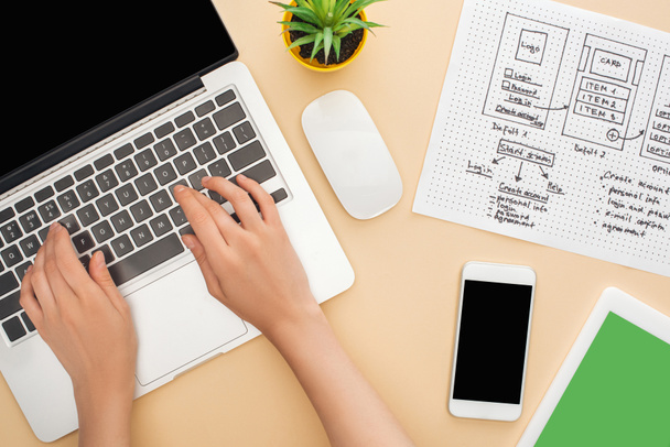 abgeschnittene Ansicht des Designers mit Laptop in der Nähe von Gadgets, Website-Design-Vorlage und grüne Pflanze auf beigem Hintergrund - Foto, Bild