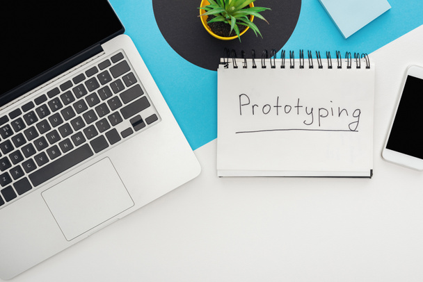 top view of laptop, smartphone, plant, notebook with prototyping lettering on abstract geometric background - Photo, Image