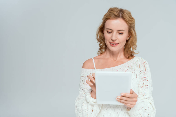 attractive and smiling woman in sweater using digital tablet isolated on grey  - Foto, afbeelding