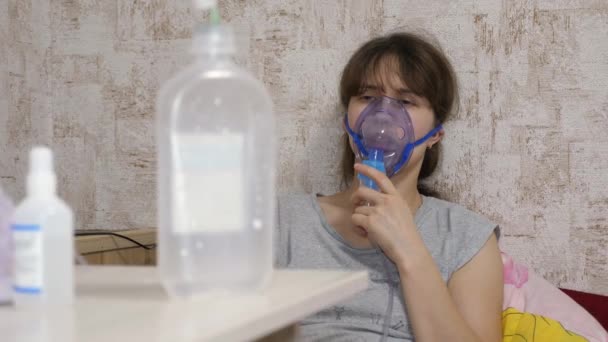 Die Frau wird mit einer Inhalationsmaske im Gesicht in einem Krankenhaus behandelt. Das kranke Mädchen wird von einem Vernebler inhaliert, der auf dem Sofa sitzt. Frau mit Maske. atmen Dämpfe für die Atemwege in die Lungen ein. Hustenbehandlung - Filmmaterial, Video