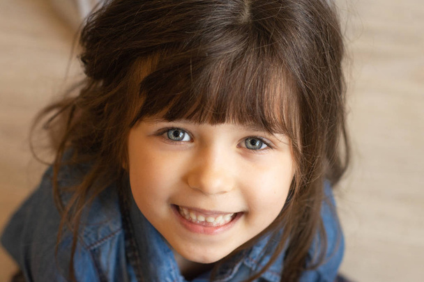 Közelíts meg egy képet a boldog gyerekről. Kislány göndör barna hajú, nagy kék szemekkel, 6-5 éves, mosolyog a kamerába. Boldog gyerekek koncepciója.  - Fotó, kép