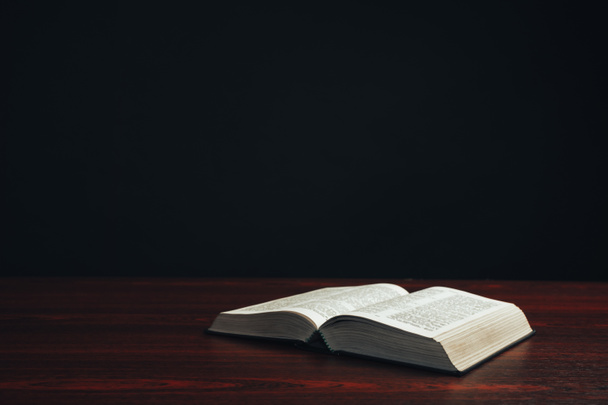 Biblia aberta em uma mesa de madeira vermelha. Belo fundo preto
. - Foto, Imagem