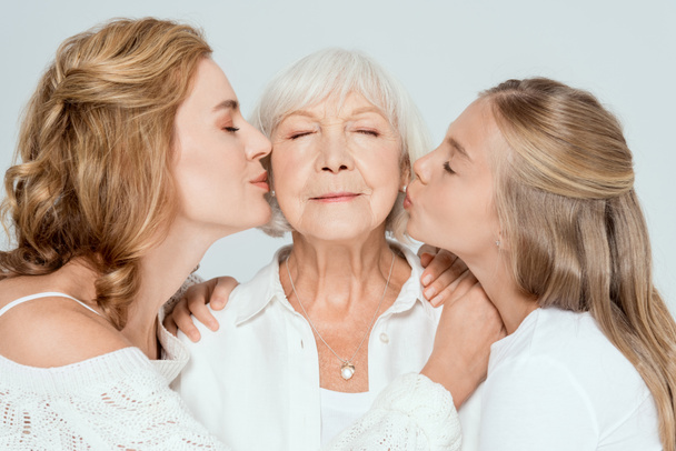 granddaughter and mother kissing grandmother with closed eyes isolated on grey  - Photo, Image