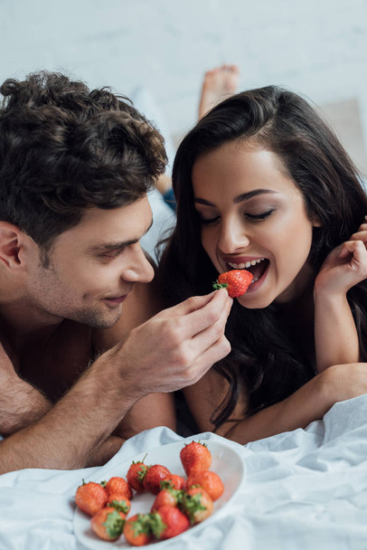 handsome man feeding attractive girlfriend with strawberry - Foto, Imagen