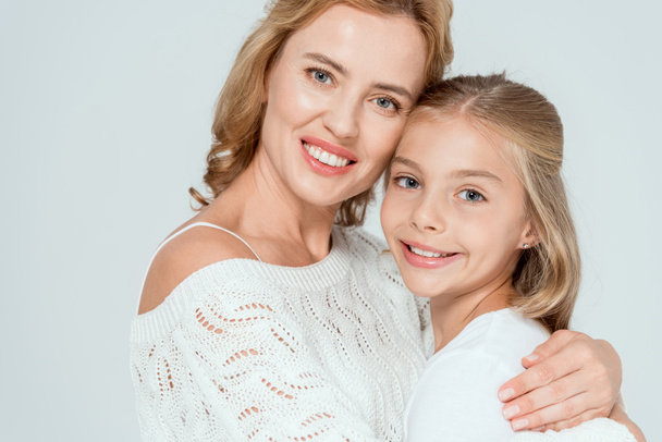 attractive mother hugging smiling daughter and looking at camera isolated on grey  - Photo, Image