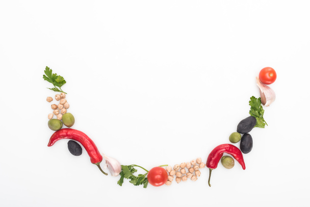 bovenaanzicht van kikkererwt, knoflook, kerstomaten, peterselie, olijven, chili peper, groene ui gerangschikt in glimlach op witte achtergrond - Foto, afbeelding