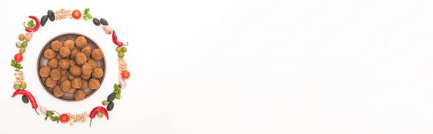 vista superior de garbanzo, ajo, tomates cherry, perejil, aceitunas, chile, cebolla verde dispuestos en marco redondo alrededor de las bolas de falafel en el plato aislado en blanco, tiro panorámico
 - Foto, imagen