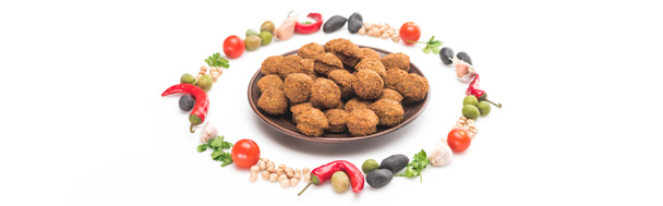 chickpea, garlic, cherry tomatoes, parsley, olives, chili pepper, green onion arranged in round frame around falafel balls on plate on white background, panoramic shot - Photo, Image
