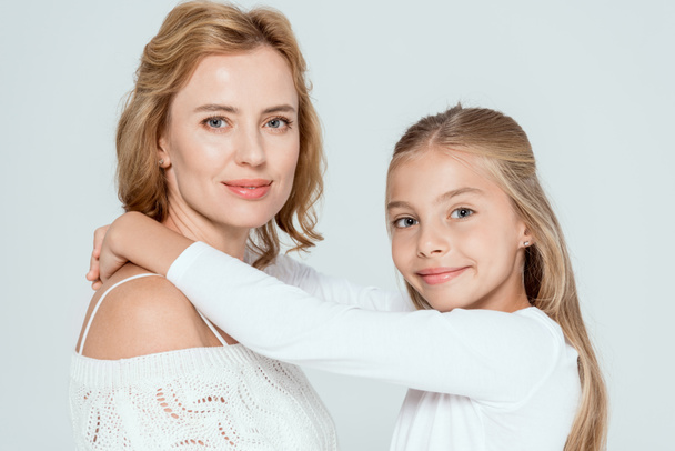 smiling daughter  hugging attractive mother and looking at camera isolated on grey  - Fotografie, Obrázek