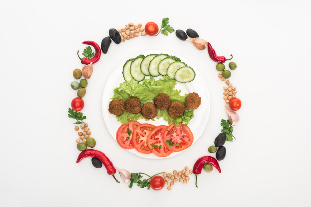 top view of vegetables arranged in round frame around falafel on plate on white background - Photo, Image