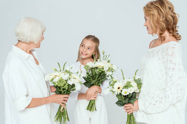 smiling granddaughter, mother and grandmother holding bouquets isolated on grey  - Fotó, kép