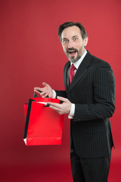 Nice purchase. Shocking discount. Mature businessman hold paper bag gift red background. Shopping concept. Christmas gift. Happy holidays. Man happy face celebrate new year. Valentines day gift - Photo, Image