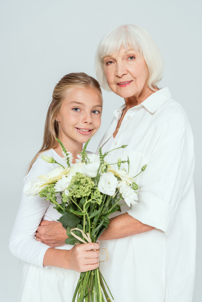 sorridente nonna che abbraccia nipote con bouquet isolato su grigio
  - Foto, immagini