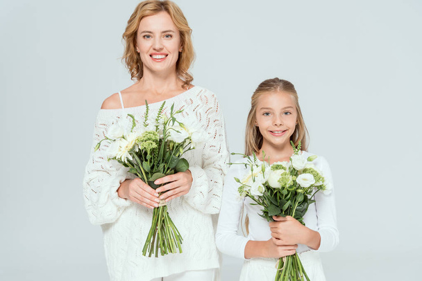 attractive mother and smiling daughter holding bouquets isolated on grey  - Fotografie, Obrázek