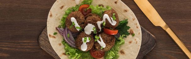 top view of falafel with vegetables and sauce on pita near knife on wooden table, panoramic shot - Фото, изображение