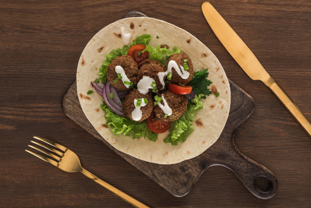 top view of falafel with vegetables and sauce on pita near cutlery on wooden table - Photo, Image