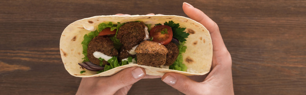 cropped view of woman holding falafel with vegetables and sauce in pita on wooden table, panoramic shot - Foto, Imagem
