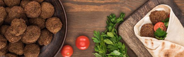vrchní pohled na falafel se zeleninou a omáčkou v pitě v blízkosti míče, petržel, rajčata na dřevěném stole, panoramatický výstřel - Fotografie, Obrázek