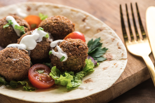 close up view of falafel with vegetables and sauce on pita on wooden table near cutlery - Foto, afbeelding