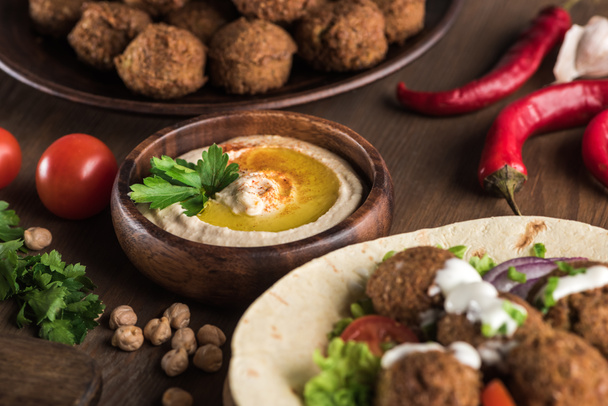 close-up zicht op falafel met groenten en saus op pita bij verse hummus op houten tafel - Foto, afbeelding