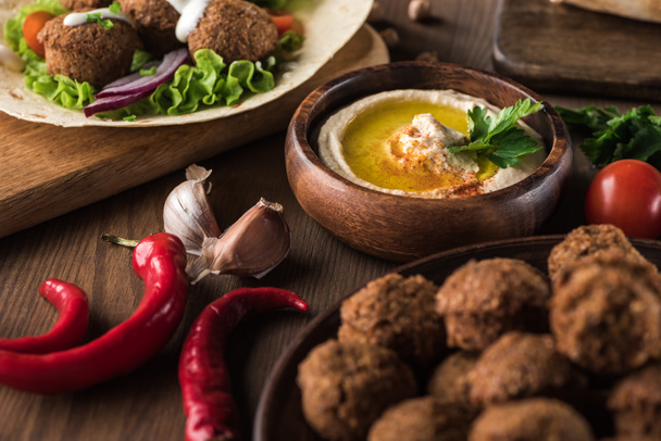 close up view of falafel near fresh hummus, spices and vegetables on wooden table - Photo, Image