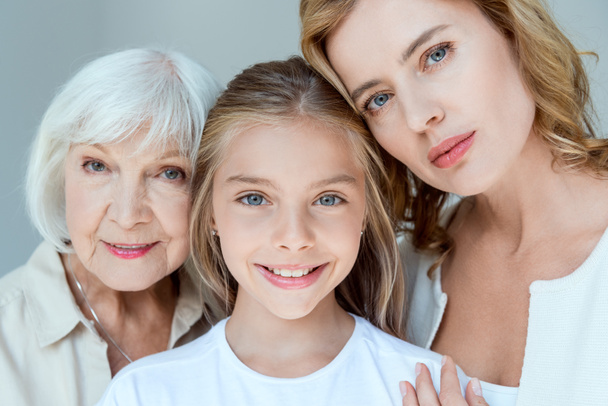 mother, grandmother and smiling granddaughter looking at camera isolated on grey  - Foto, Imagen